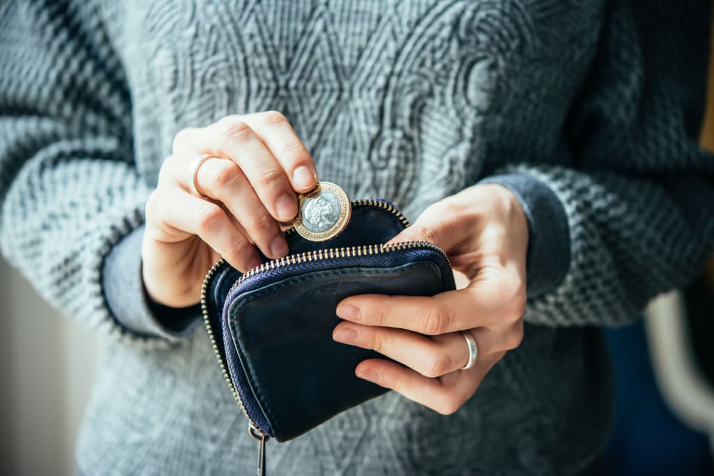 Person holding pound coin and small purse, symbolising savings